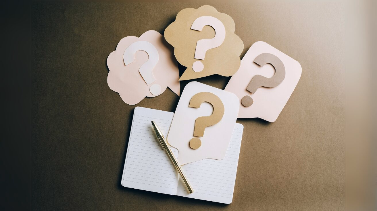 Paper question marks and a note pad and pen
